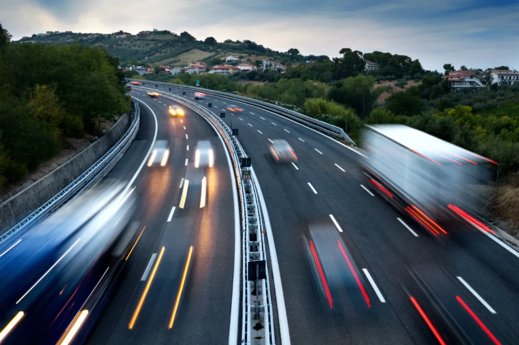Trucks and cars moving quickly on a highway through a scenic countryside.
